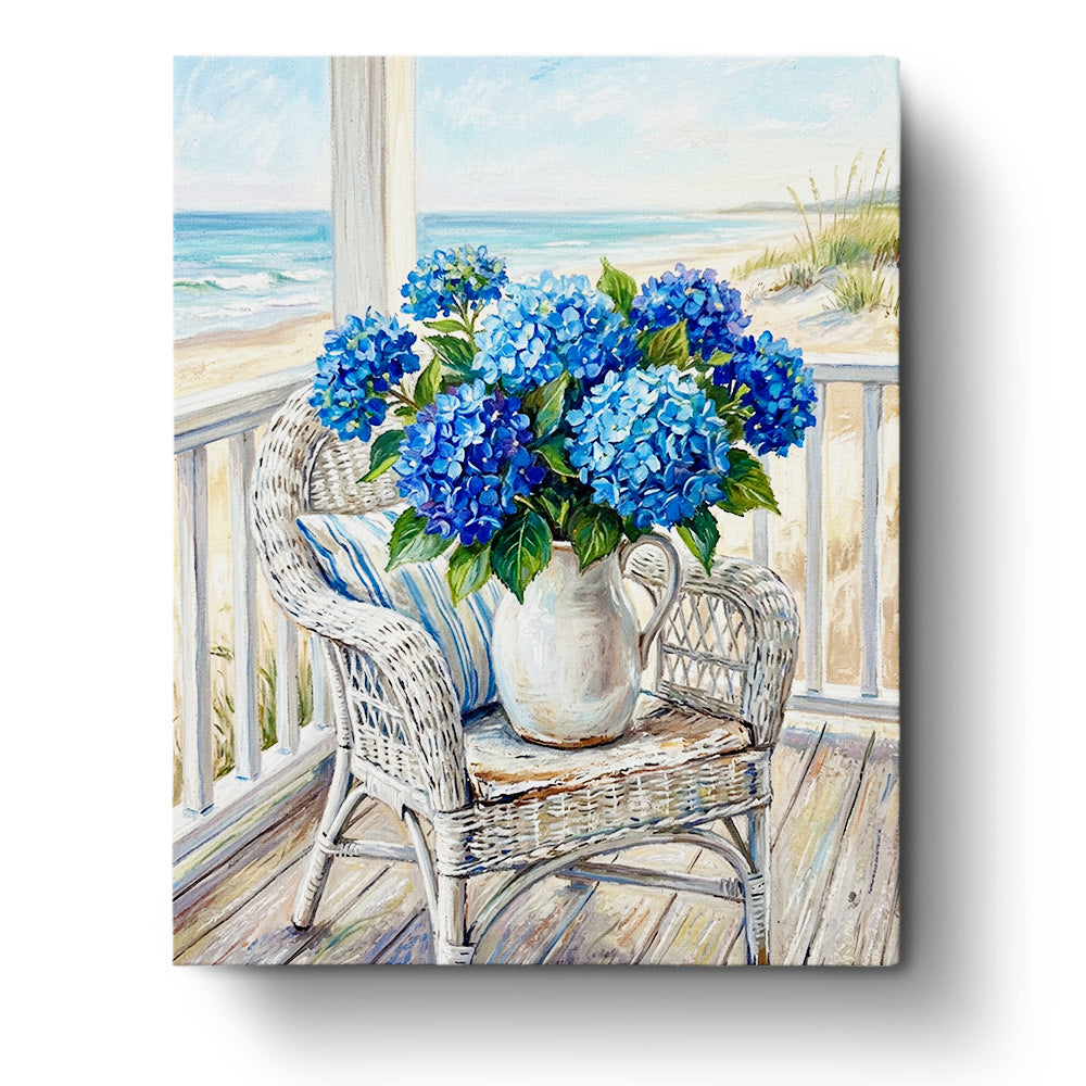 Blue Hydrangeas by the Sea paint by numbers kit from BestPaintByNumbers. A wicker chair with a vase of vivid blue hydrangeas, set against a calming coastal view, emphasizing mindfulness and creativity.