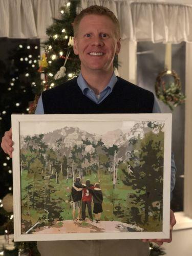 A men is holding a self painted picture that he painted with a paint by number kit. Christmas tree in background.